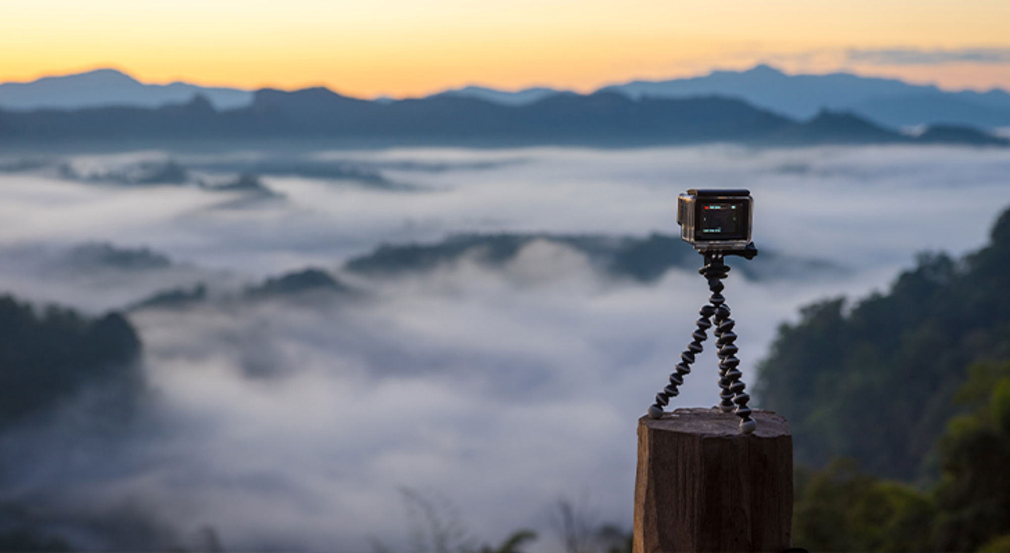 Cadeau voor reiziger GoPro Actioncamera op statief bij zonsopkomst boven een mistige vallei en bergsilhouetten.