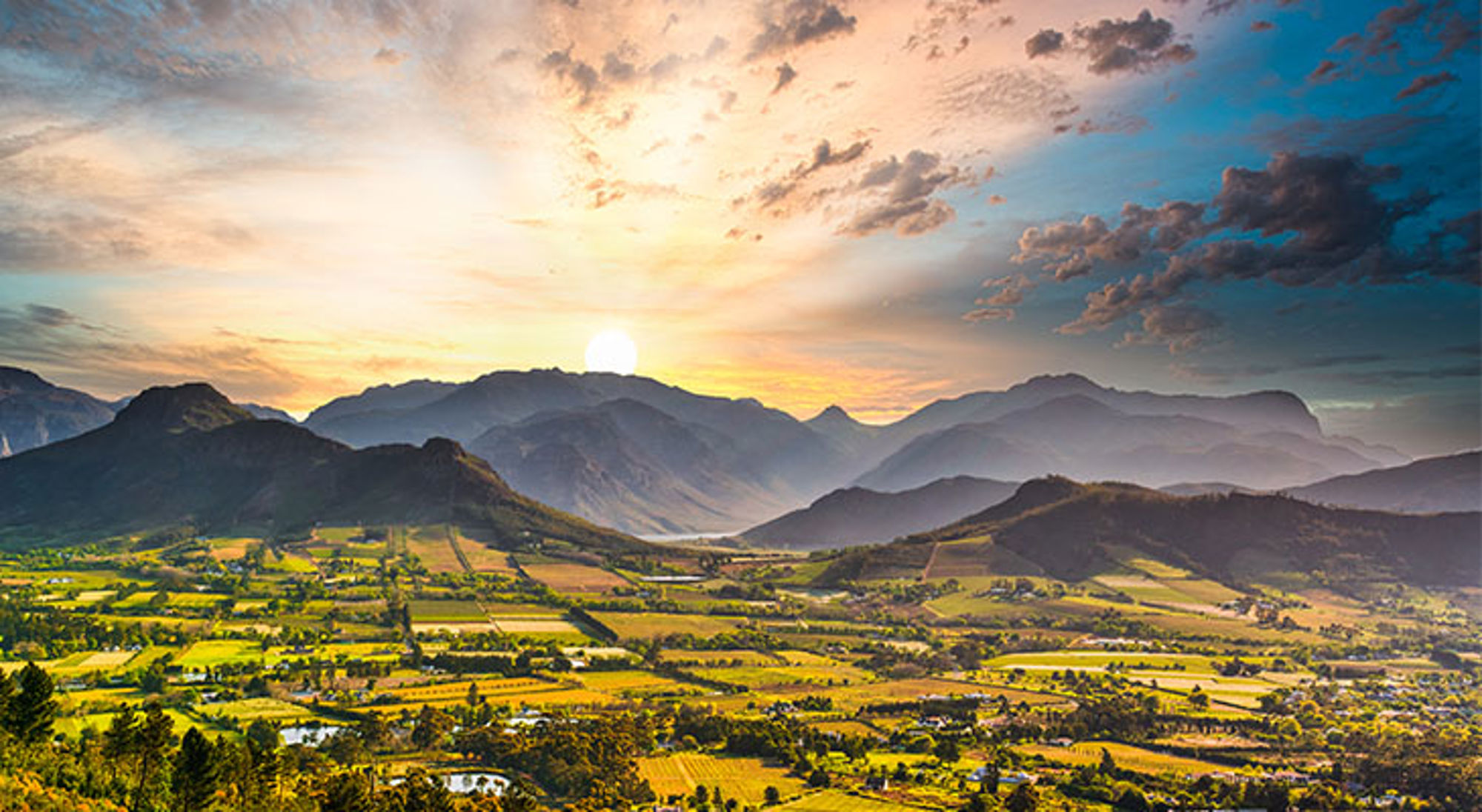 Zonsondergang in Franschhoek Zonsondergang boven groene wijngaarden en bergen in de Kaapse Wijnlanden, Zuid-Afrika.