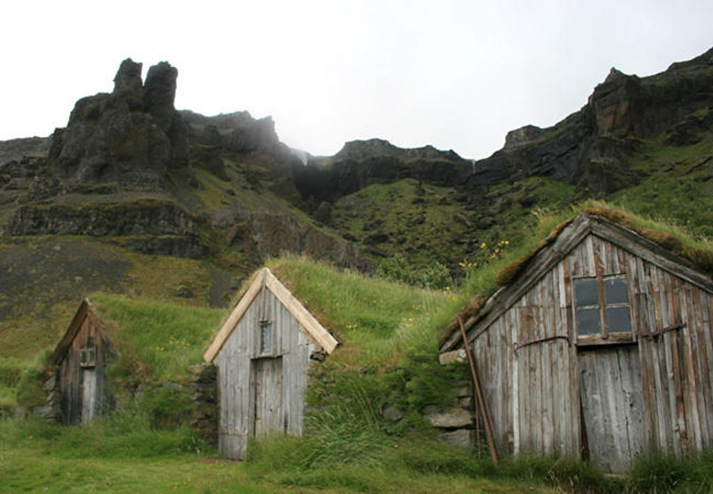Traditionele turfhuisjes in groen IJslands landschap met rotsachtige bergen op de achtergrond.