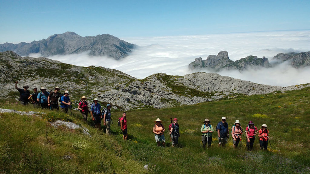 Wandelaars in de Picos de Europa tijdens een wandelvakantie in Spanje, met bergtoppen boven een wolkendek.