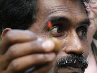 Close-up van een man die een kleine rode bloemknop vasthoudt tijdens de route door Zuid-India.