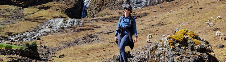 Wandelaar in de Peruaanse Andes met waterval en grazende lama’s op de achtergrond.