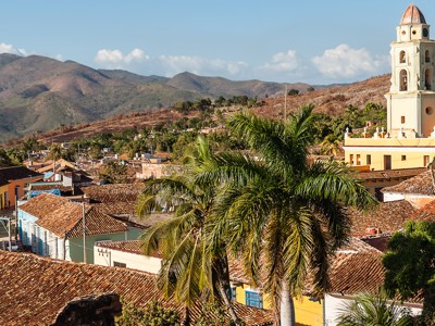 Uitzicht over Trinidad in Cuba met kleurrijke daken, palmbomen en de kerktoren, met bergen op de achtergrond.