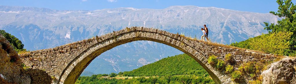 Wandelaars op een oude stenen boogbrug in de bergen van Albanië tijdens een familiereis.