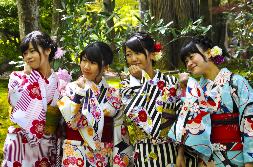 Vier vrouwen in kleurrijke kimono’s poseren in een groene Japanse tuin tijdens een familiereis Japan.