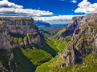 Uitzicht over de Vikoskloof in Griekenland, met steile rotswanden en groene vallei onder een blauwe lucht.