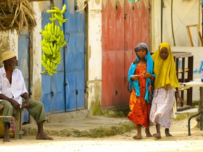 Twee meisjes lopen langs kleurrijke deuren in Stone Town, Zanzibar, met bananen aan een gevel.