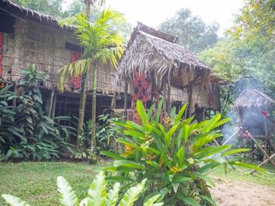 Traditioneel langhuis met rood houtsnijwerk in het regenwoud van Maleisisch Borneo tijdens de familiereisroute.