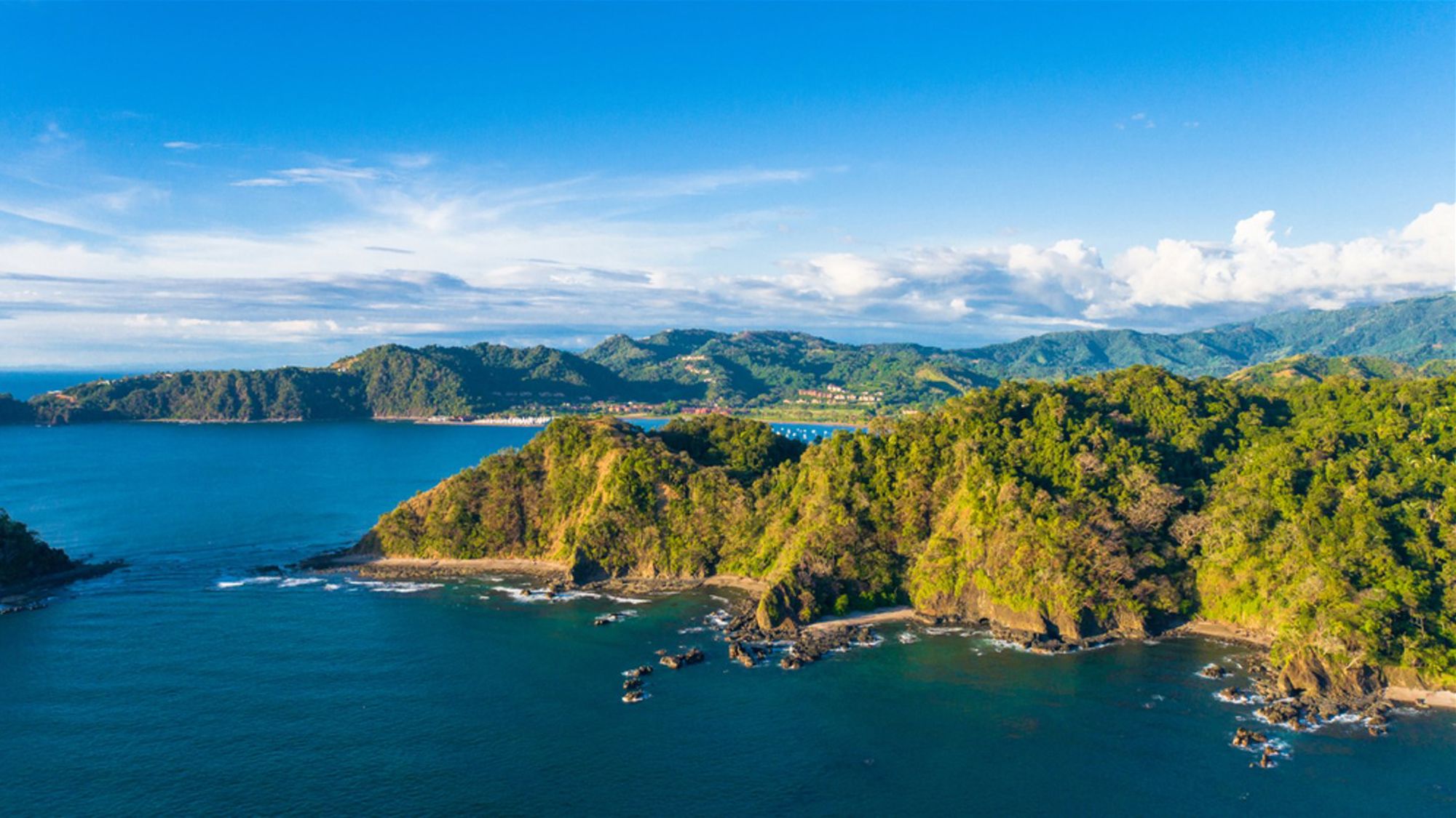 Groene kustlijn met baaien en heuvels aan de Pacifische kust van Costa Rica onder een blauwe lucht.