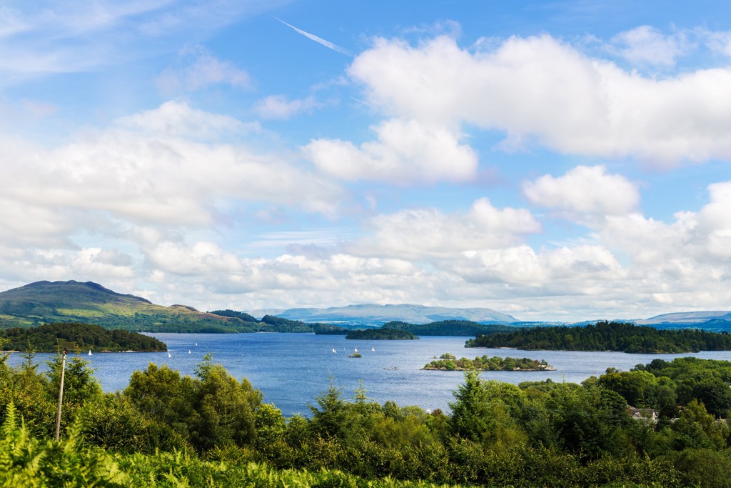 Uitzicht over Loch Lomond met groene heuvels en zeilboten tijdens een groepsrondreis door het Verenigd Koninkrijk.