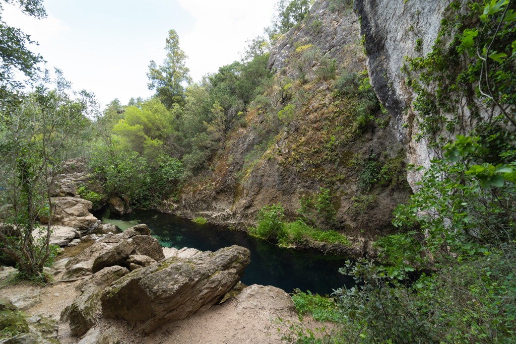 Groene kloof met rotswanden en een helderblauwe rivier, wandelroute op Sardinië, Italië.