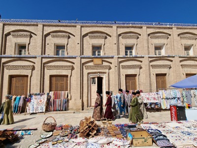 Markt met kleurrijke textiel en lokale handelaren voor een historisch gebouw langs de Zijderoute.