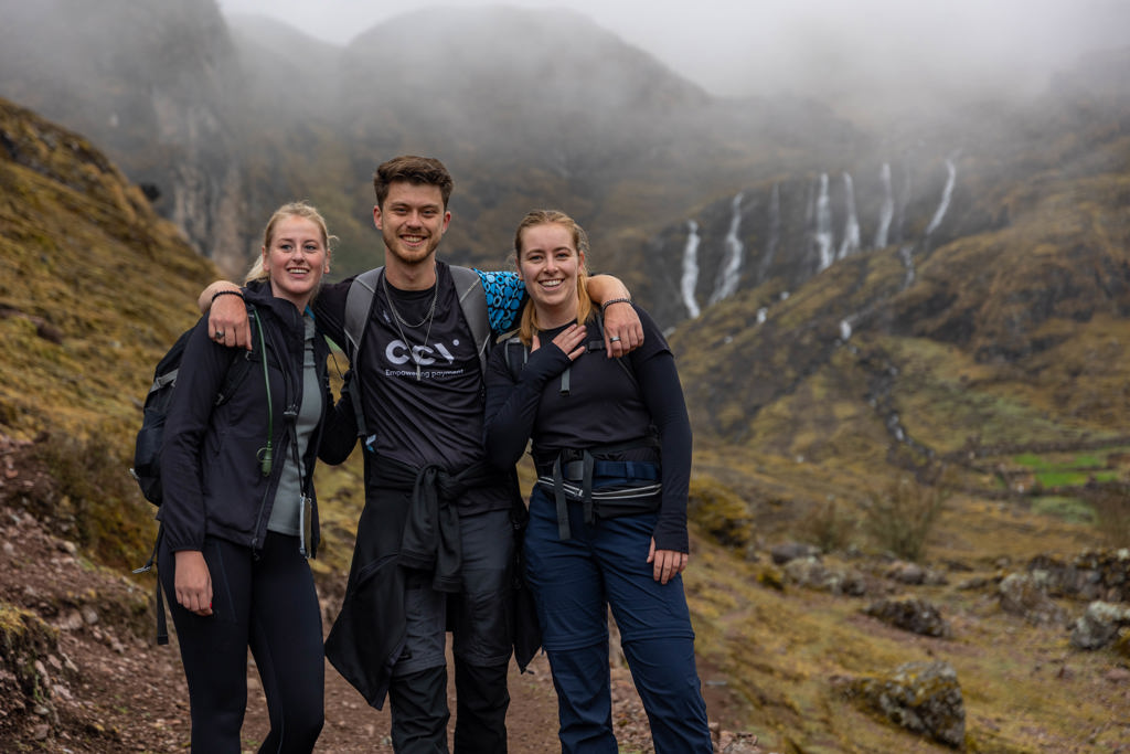 22-35ers groepsreis Peru: drie hikers op bergpad met watervallen op de achtergrond.