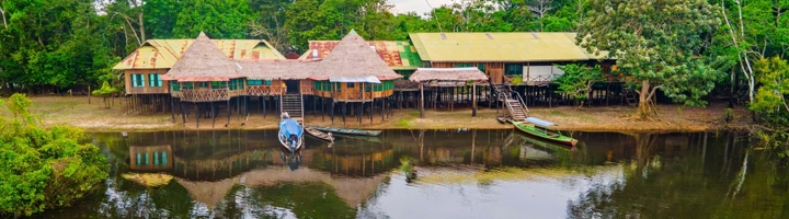 Lodges op palen aan de rivier in de Amazone in Colombia, met boten aan de oever.