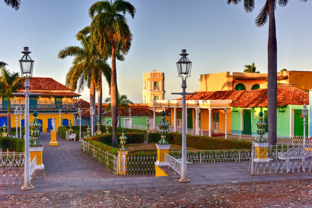 Kleurrijke straat in Trinidad, Cuba, met palmbomen, lantaarns en huizen met rode dakpannen.