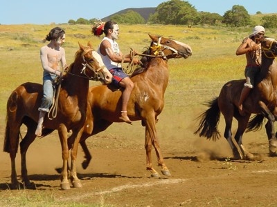 Rapa Nui ruiters met geschminkte gezichten racen te paard over een stoffig veld tijdens een festival.
