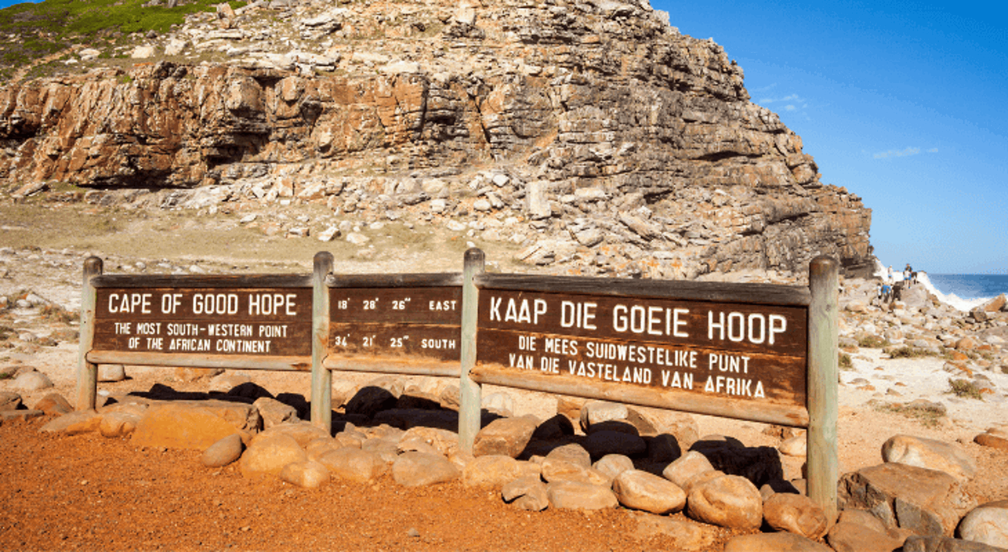 Kaap de Goede Hoop Houten bord met “Cape of Good Hope” bij Kaap de Goede Hoop, met rotsachtige kust en blauwe lucht.