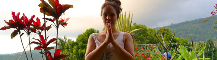 Vrouw met gevouwen handen in een tropische tuin op Bali, met groene heuvels op de achtergrond.
