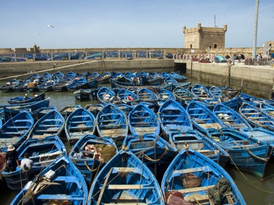 Blauwe vissersbootjes in de haven van Essaouira, Marokko, met oude vestingmuur op de achtergrond.