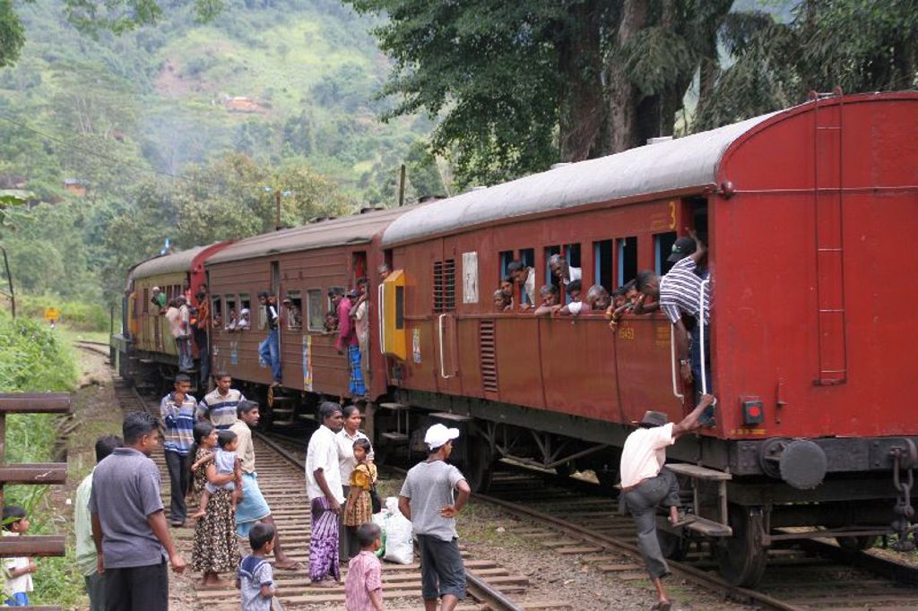 Lokale trein in Sri Lanka met reizigers langs het spoor, omringd door groene heuvels.