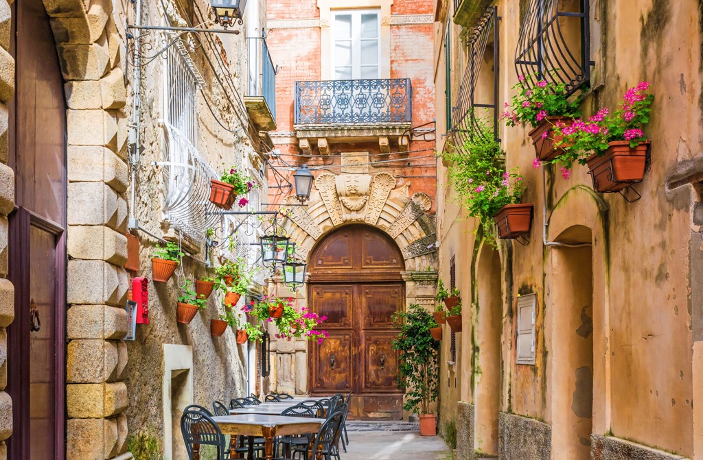 Sfeervol steegje aan de Amalfikust met terrastafels, balkons en bloeiende bloemen in Italië.