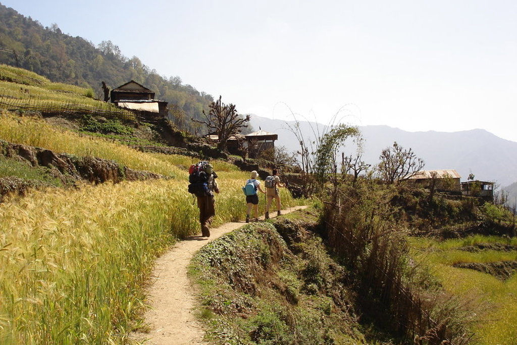 Gezin wandelt met rugzakken over een bergpad langs terrassen en dorpjes tijdens familiereis Nepal.