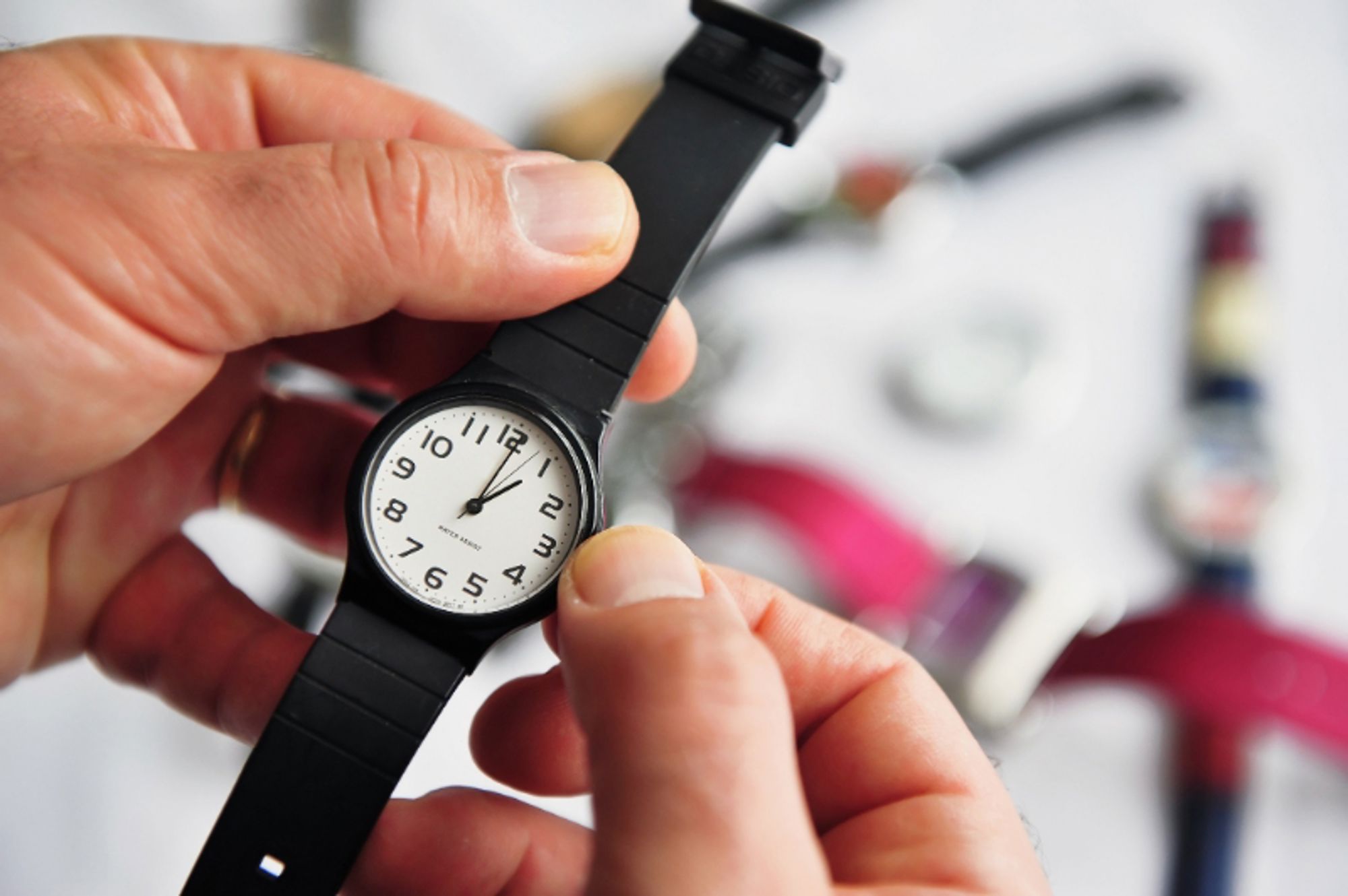 Tijd verzetten Handen die een zwart horloge met witte wijzerplaat vasthouden, met reisbenodigdheden onscherp op de achtergrond.