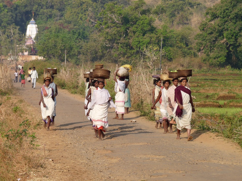 Dorpsbewoners lopen over een landweg in Orissa, India, met manden en bagage op het hoofd.