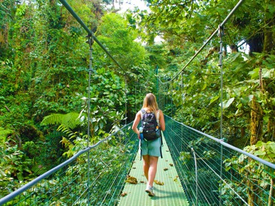 Wandelaar met rugzak op hangbrug door het nevelwoud in Costa Rica tijdens de 22-35ers reis.