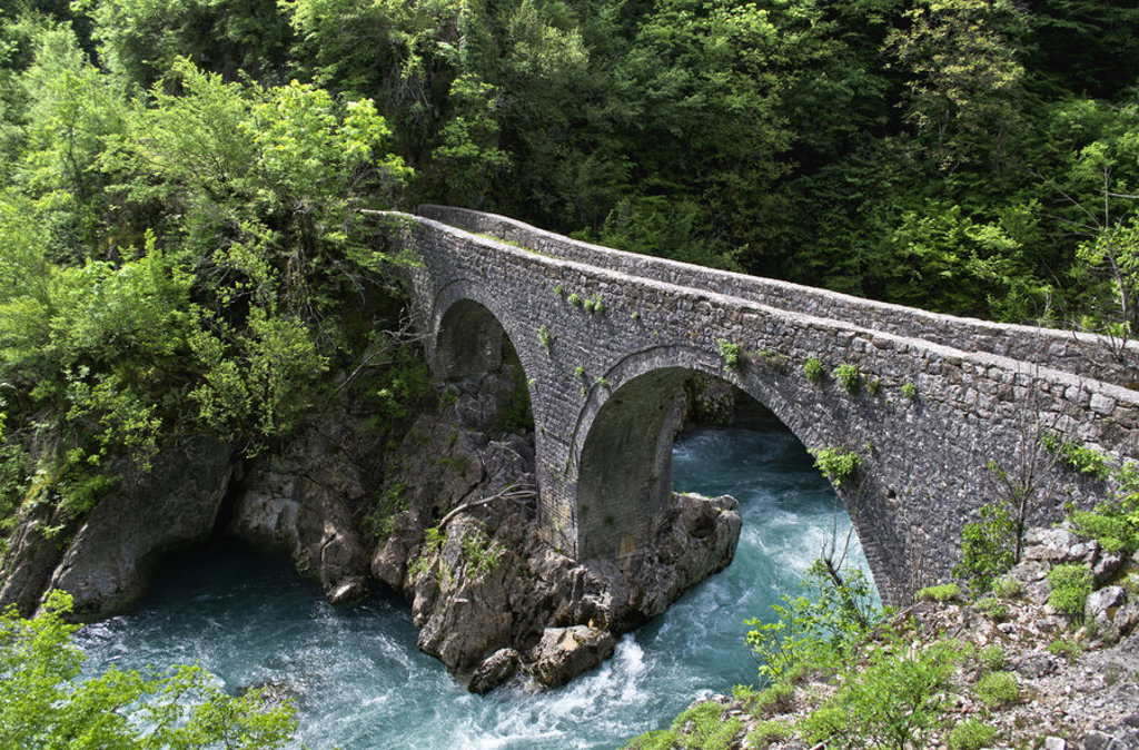 Oude stenen boogbrug over een turquoise rivier in een groene kloof tijdens de groepsrondreis Balkan.