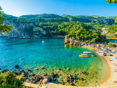 Turquoise baai met strand en bootjes op Corfu, onderdeel van de Route Zuidoost Europa.