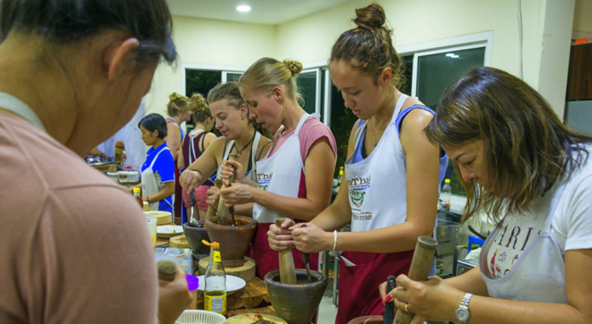 Kookworkshop met deelnemers die ingrediënten fijnstampen in vijzels in een Thaise keuken.