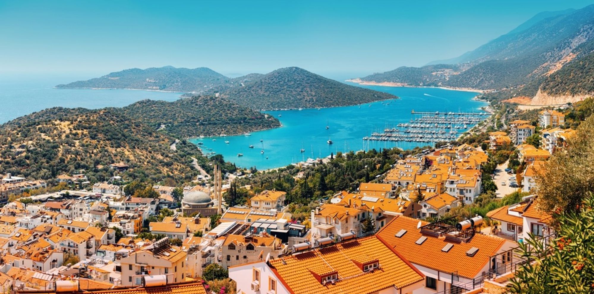 Uitzicht op de jachthaven en baai van Kaş aan de Turkse Rivièra, met oranje daken en bergen op de achtergrond.