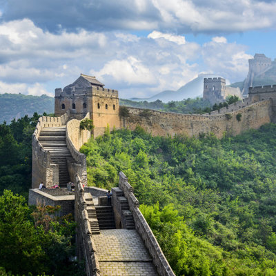 De Chinese Muur slingert over groene bergen onder een blauwe lucht, tijdens een groepsrondreis China.