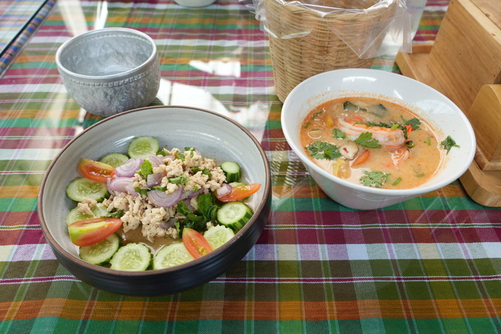 Thaise maaltijd met tom yum-soep en salade op een geruite tafel, familiereis Thailand Comfort-Plus.