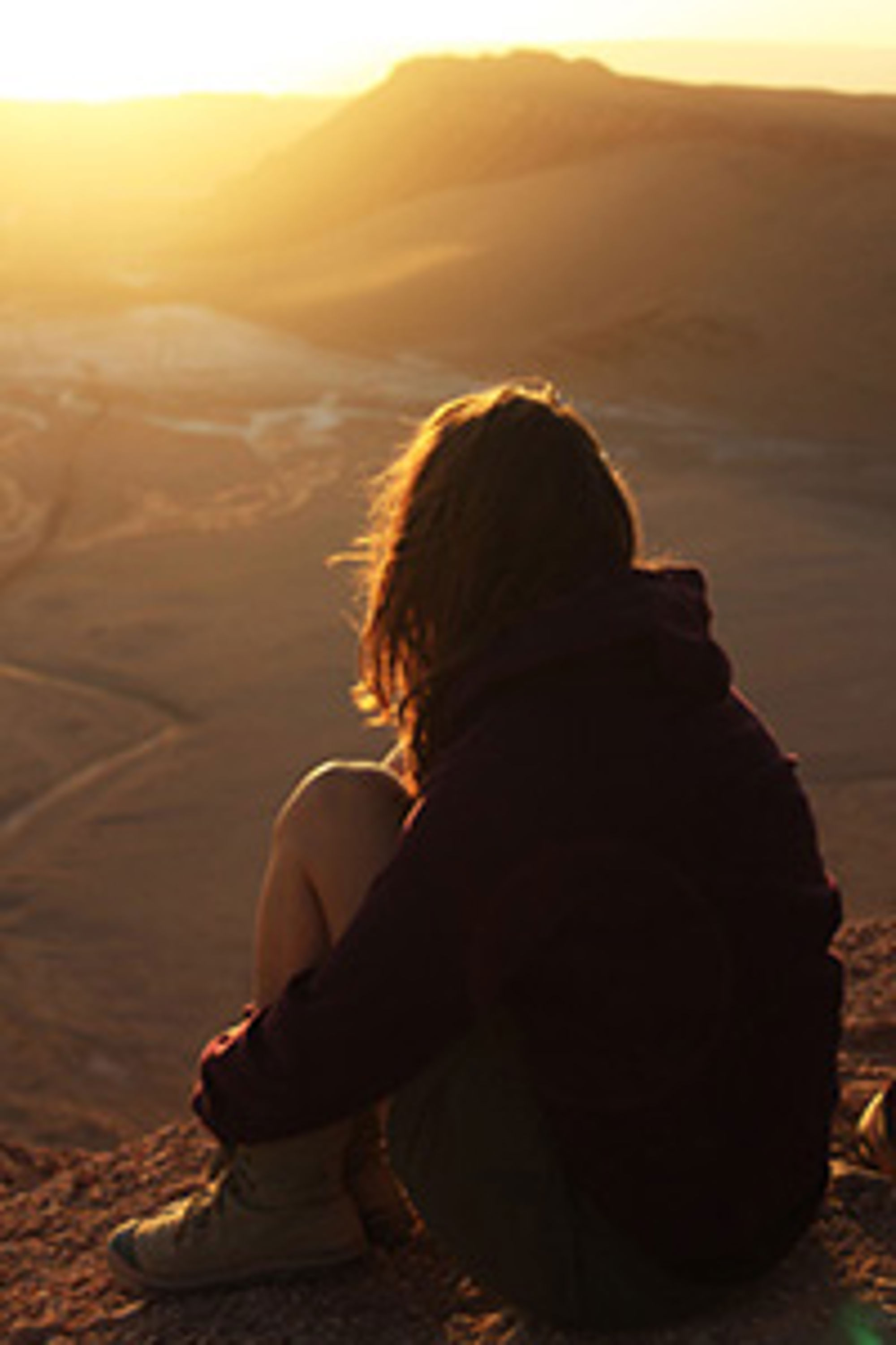 Atacama-woestijn, Chili Persoon zit op een rots en kijkt bij zonsondergang uit over een bergachtig landschap.