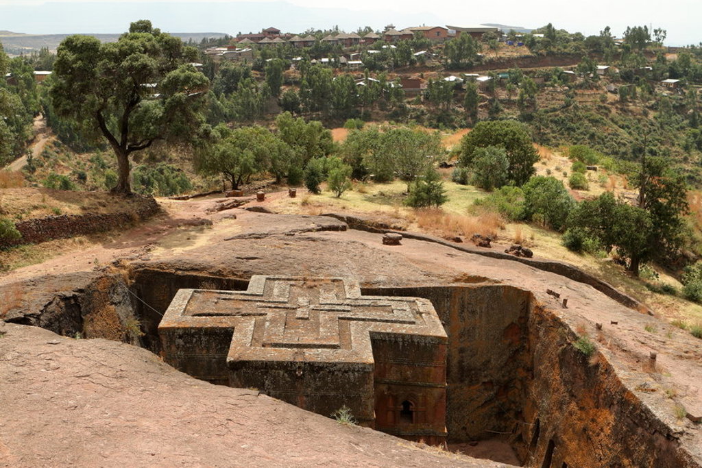 Uit rots gehouwen kerk in kruisvorm in Lalibela, Ethiopië, omringd door groen heuvelandschap.