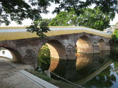 Oude stenen boogbrug over een rustige rivier in Cuba, met weerspiegeling in het water.