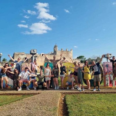 Groep reizigers tijdens 22-35ers reis Mexico bij kleurrijke muurschildering en historische ruïnes.