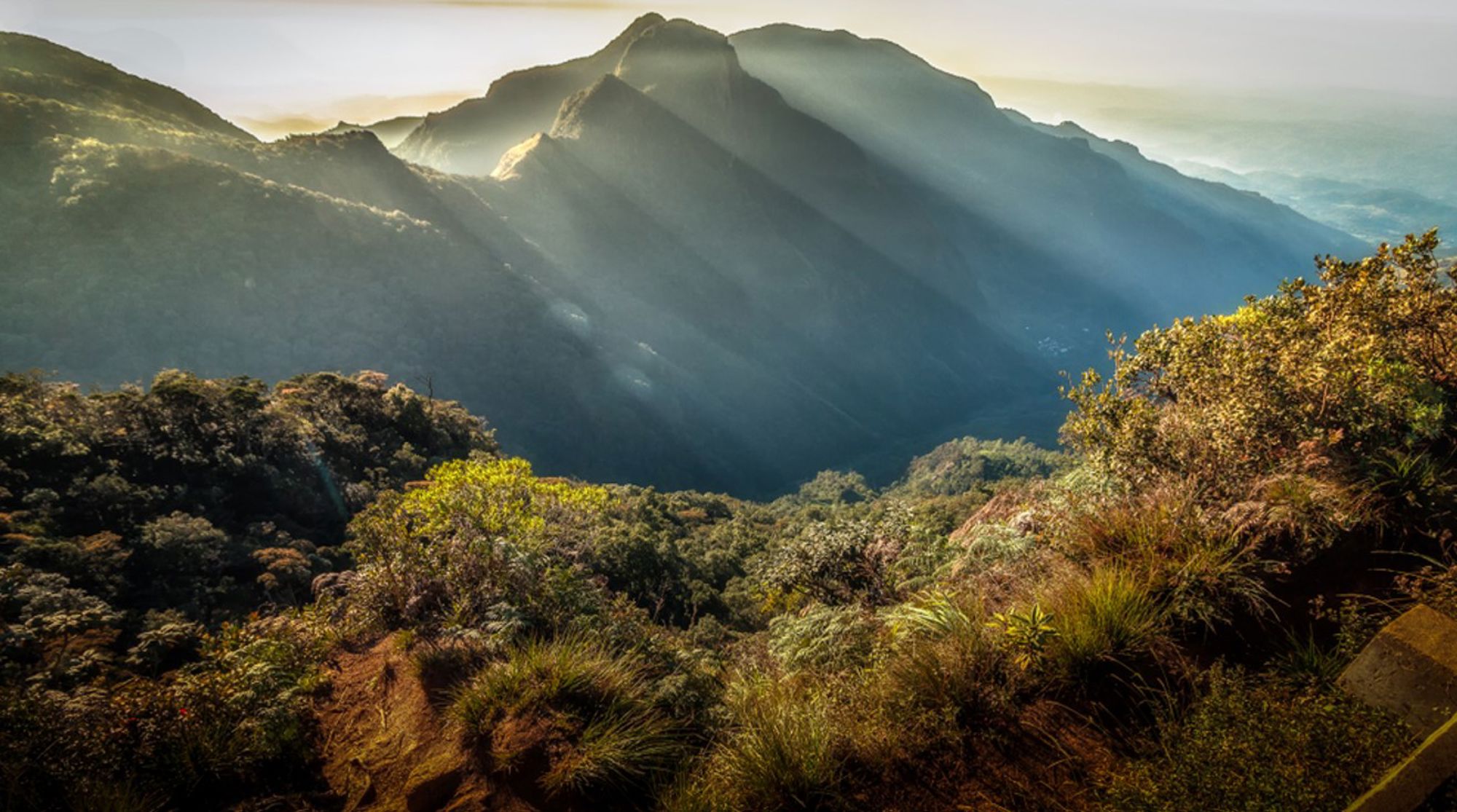 Zonsopkomst boven de Sri Lankaanse bergen, met zonnestralen over een groen berglandschap.