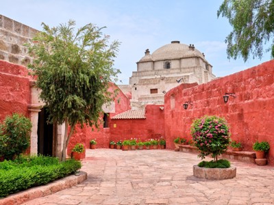 Binnenplaats van het Santa Catalina-klooster in Arequipa met rode muren, bloemen en koepel op de achtergrond.