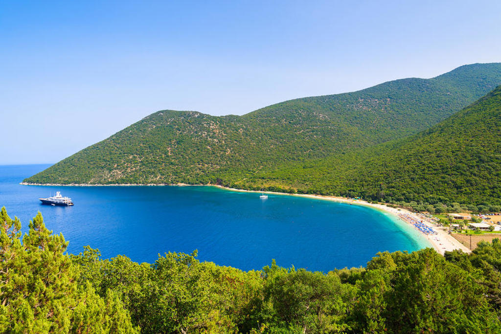 Groene heuvels en zandstrand aan een blauwe baai in Griekenland tijdens de meivakantie.