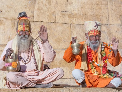Sadhu’s in Noord-India met gezichtsverf en gebedskralen, zittend bij een tempelmuur en zegenend.