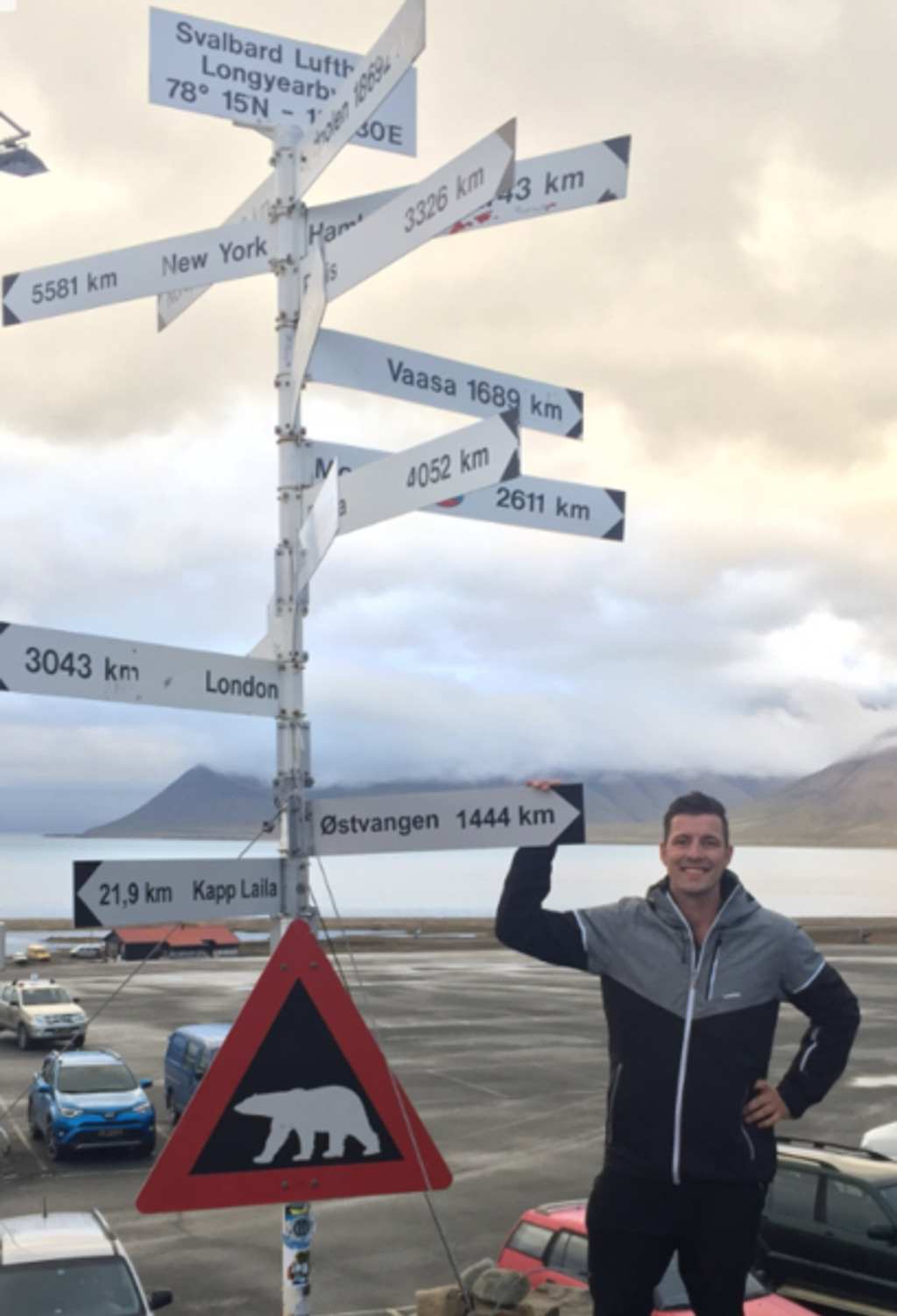 Wegwijzer in Longyearbyen, Spitsbergen, met ijsbeerwaarschuwingsbord en reiziger op de voorgrond.