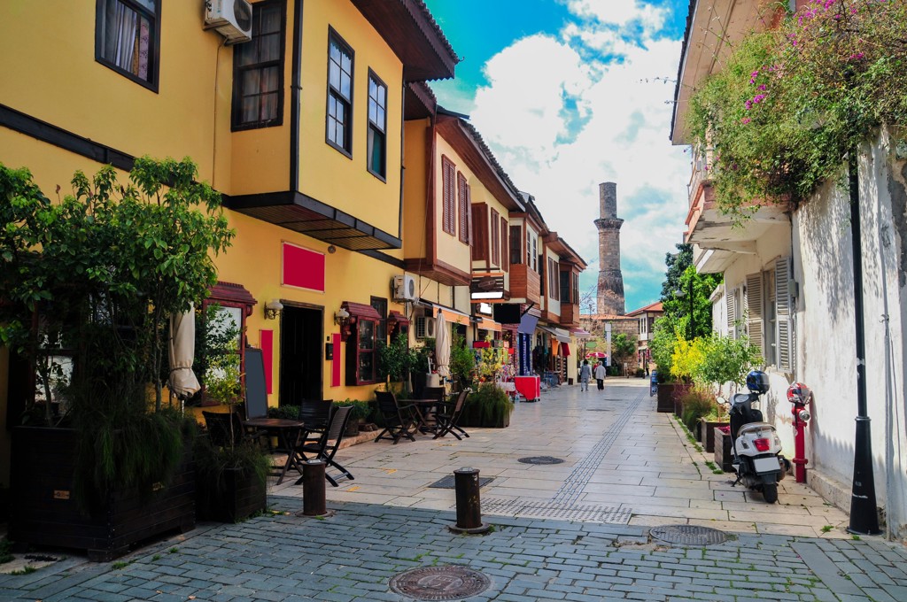 Sfeervolle straat in Istanbul met Ottomaanse huizen, terrasjes en een minaret op de achtergrond.