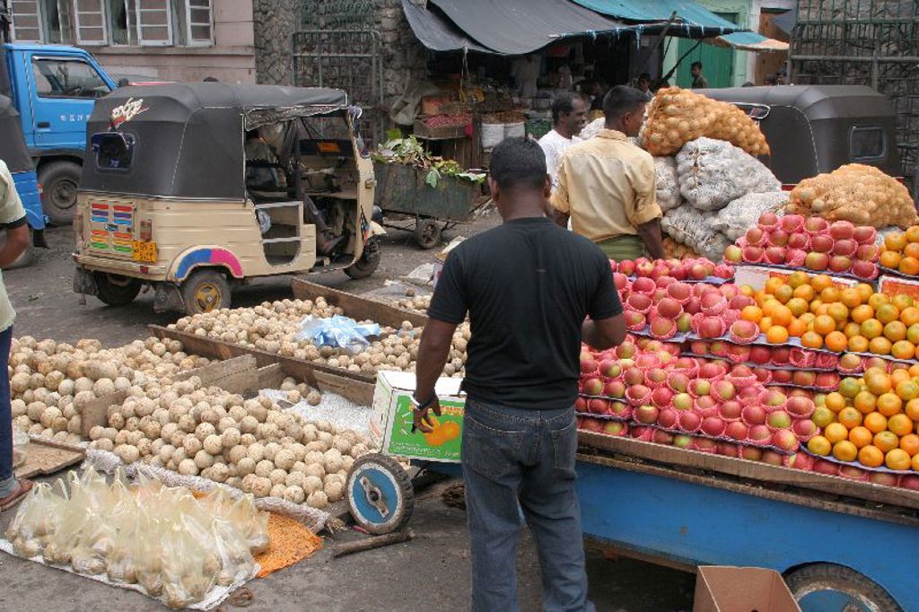 Markt in Sri Lanka met fruitkramen, zakken uien en tuktuks tijdens een groepsrondreis langs hoogtepunten.