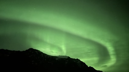 Groen noorderlicht boven een donker berglandschap in IJsland tijdens een winterreis.