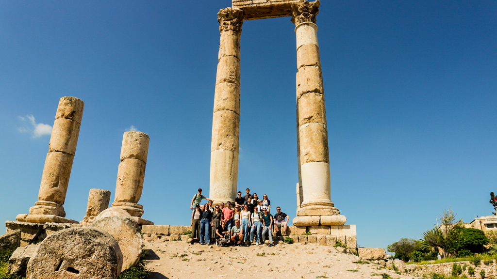 Groep 22-35ers reizigers bij Romeinse zuilen in Jordanië onder een helderblauwe lucht.