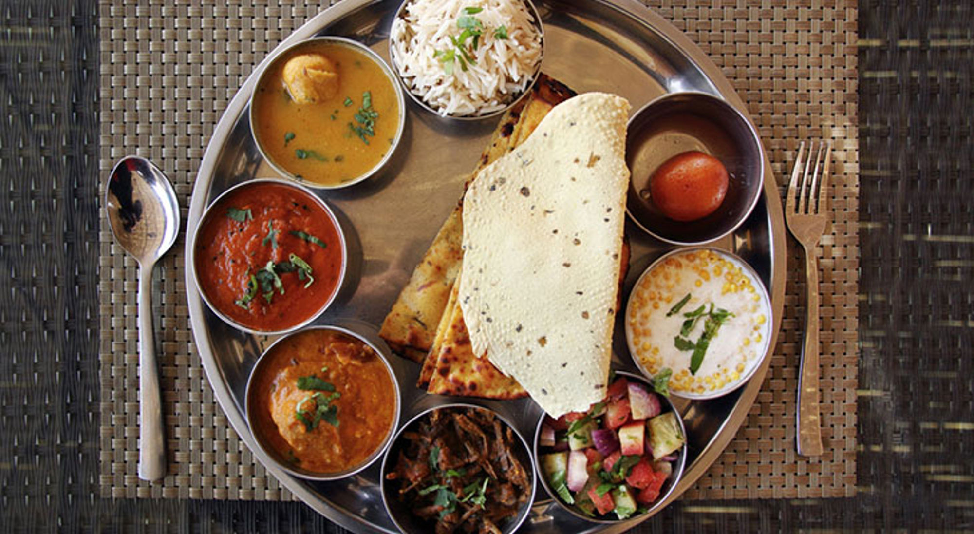 Vegetarisch Indisch gerecht Traditionele Indiase thali met curry’s, rijst, naan, salade en dessert op een metalen schaal.