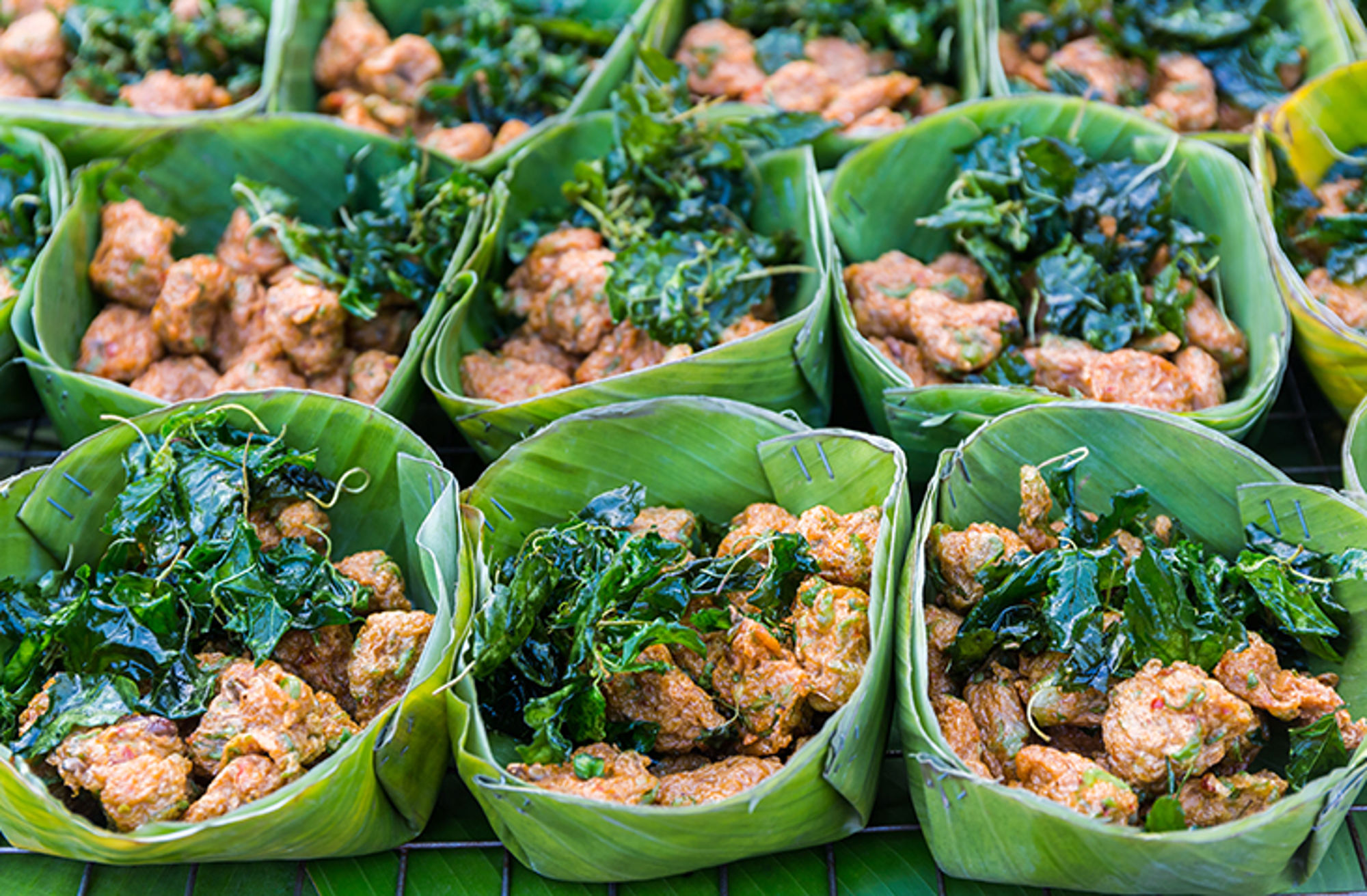 Thaise viskoekjes in bananenblad met verse kruiden op een markt.